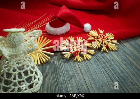 Natale rustico ancora in vita con paglia artigianali di ornamenti, una festa di Santa Red Hat, matching tessuto rosso e spighe di grano dorati su un di legno backgr Foto Stock