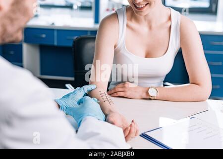 Vista ritagliata della allergist tenendo la siringa vicino a donna felice in clinica Foto Stock