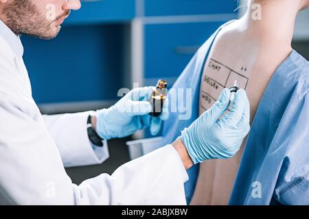 Vista ritagliata del barbuto allergist pipetta tenuta nei pressi di donna con lettere sul marcato indietro Foto Stock