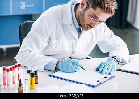 Messa a fuoco selettiva del barbuto immunologist in bicchieri tenendo la penna vicino negli appunti Foto Stock
