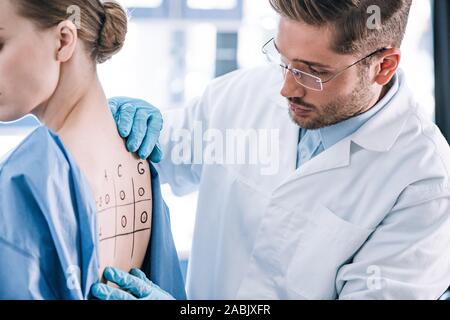 Bello allergist in piedi vicino a donna e toccando nuovamente contrassegnati con numeri e lettere Foto Stock