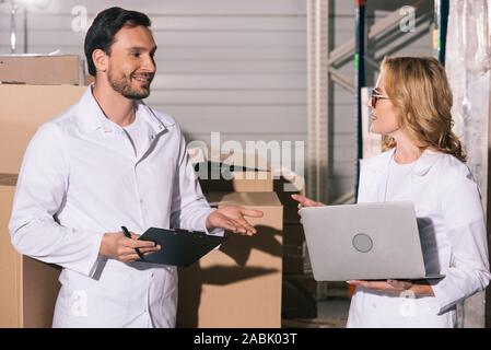 Bello ammassatore parlando a un collega azienda laptop in magazzino Foto Stock