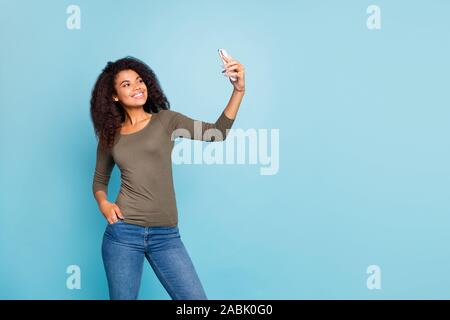 Ritratto di affascinante allegro positivo afro american girl avente tempo libero sul cammino tenendo selfie chiamata video per il suo blog usura informale in stile denim Foto Stock