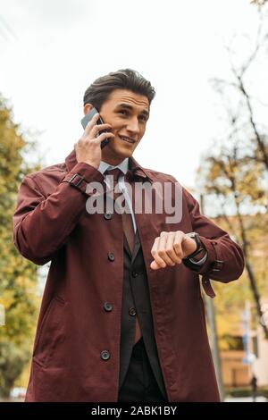 Imprenditore parlando su smartphone e controllare il tempo su un orologio da polso sulla strada Foto Stock