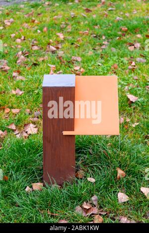 Arancio bianco tavola di legno per informazioni e indicazioni nel parco, con uno sfondo di erba verde coperta da foglie di autunno Foto Stock