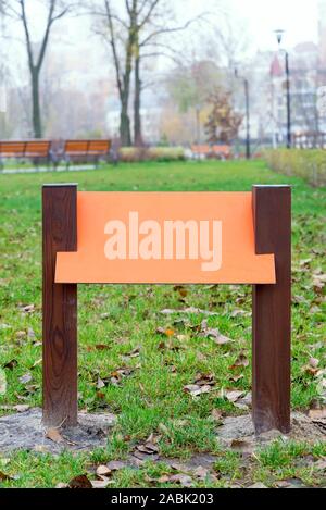 Arancio bianco tavola di legno per informazioni e indicazioni nel parco, con uno sfondo di erba verde coperta da foglie di autunno Foto Stock