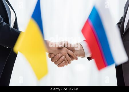 Vista ritagliata di diplomatici stringono le mani nei pressi di ucraini e russi bandiere Foto Stock