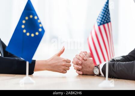 Vista ritagliata del diplomatico dell'Unione europea mostra il pollice fino nei pressi di ambasciatore degli Stati Uniti d'America seduto con le mani chiuse Foto Stock