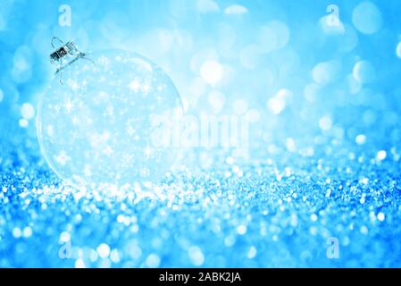 Trasparente palla di Natale con il simbolo del fiocco di neve contro glitter blu luminoso dello sfondo. Foto Stock