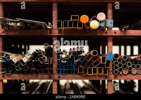 Un dettaglio di diversi stili e dimensioni del vecchio metallo riciclato di tubi e profili dei materiali da costruzione la posa sul ripiano di un rack in un magazzino riciclato m Foto Stock