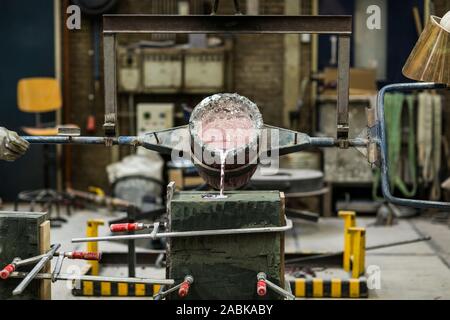 Metallo sabbia tecnica di colata colata di alluminio fuso colore argento liquido in uno stampo in un ambiente industriale, spazio officina Foto Stock