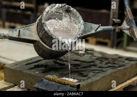 Metallo sabbia tecnica di colata colata di alluminio fuso colore argento liquido in uno stampo in un ambiente induastrial, spazio officina Foto Stock