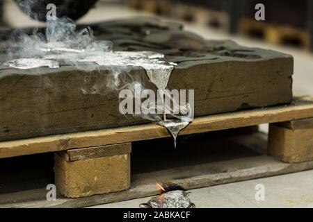 Metallo sabbia tecnica di colata colata di alluminio fuso colore argento liquido in uno stampo mentre si effettua il fumo in un ambiente industriale, spazio officina Foto Stock