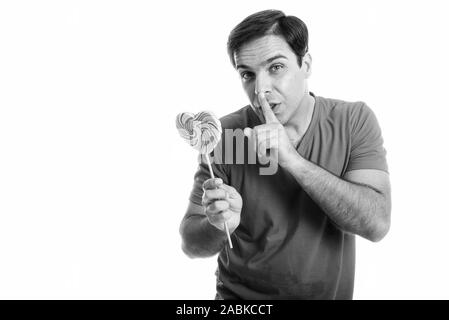Studio shot del giovane uomo persiano di contenimento a forma di cuore lecca-lecca con il dito sulle labbra isolata contro uno sfondo bianco Foto Stock