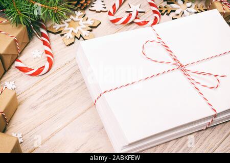 Busta con foglio di carta bianco su sfondo di Natale - ramo di abete, pigne, nastro rosso, stella e il cuore di dolci. Spazio per il testo. Tonica. Foto Stock