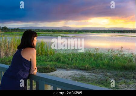 Turista femminile, al tramonto, appoggiato sulla piattaforma di osservazione rampa, presso il San Lorenzo le zone umide, nei pressi di Mackay, Queensland, Australia. Foto Stock