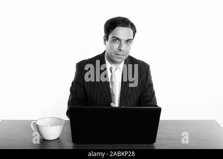 Studio shot di imprenditore persiano seduta con il computer portatile e la tazza di caffè sul tavolo in legno Foto Stock