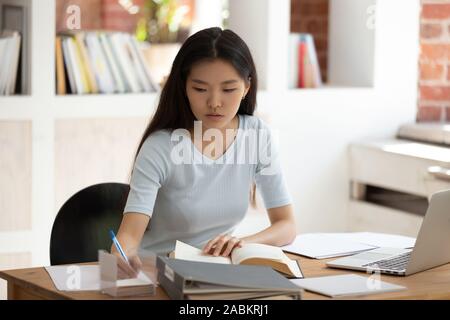 Concentrato di giovani asiatici studentessa seduti alla scrivania in libreria. Foto Stock