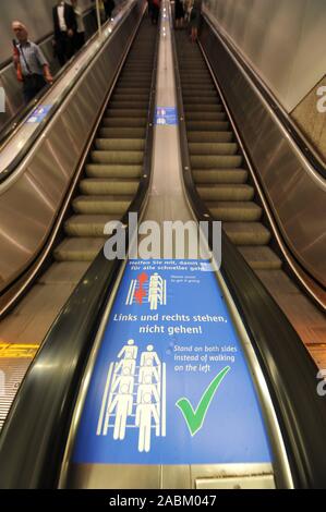 Una nuova etichetta con le parole " stand di sinistra e di destra non vanno! Ci aiutano a rendere le cose andare più veloce" è il blasonato su due scale mobili al centro della piattaforma di linee della metropolitana 1 e 2 alla stazione centrale di Monaco. [Traduzione automatizzata] Foto Stock