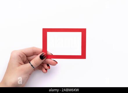 Womans mano con manicure tenendo la cornice rossa isolato su sfondo bianco. Laici flat top view mockup Foto Stock