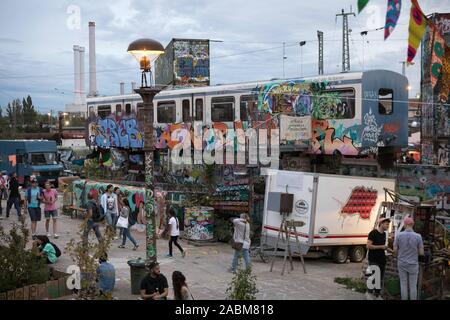 I visitatori del festival estivo di fronte un scartato carro ferroviario e vecchi contenitori spruzzata con graffiti. [Traduzione automatizzata] Foto Stock