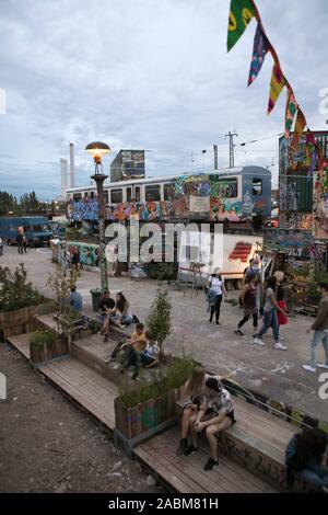 I visitatori del festival estivo di fronte un scartato carro ferroviario e vecchi contenitori spruzzata con graffiti. [Traduzione automatizzata] Foto Stock