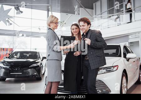 Gli orgogliosi possessori. Giovane e bella coppia felice costeggiata in piedi accanto a loro appena acquistato auto con gioia la sorridente che mostra le chiavi dell'auto alla telecamera copyspace Foto Stock