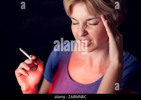 La donna fuma sigarette e ha un forte mal di testa. Il tabagismo e il problema della salute concetto Foto Stock