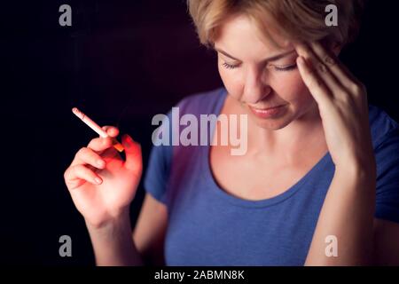 La donna fuma sigarette e ha un forte mal di testa. Il tabagismo e il problema della salute concetto Foto Stock