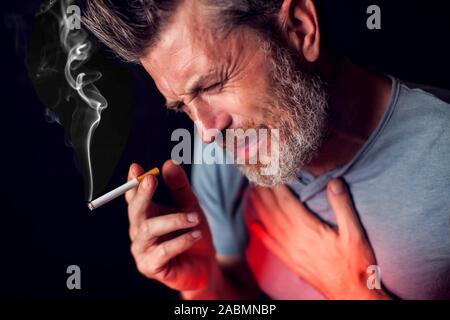 L'uomo fuma sigarette e ha problemi con i polmoni nella parte anteriore del fondo nero. Dipendenza dalle sigarette concept Foto Stock