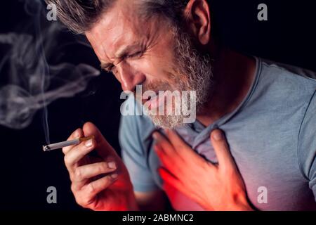 L'uomo fuma sigarette e ha problemi con i polmoni nella parte anteriore del fondo nero. Dipendenza dalle sigarette concept Foto Stock