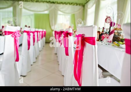 Bellissimo set di nozze decorazione nel ristorante. Rosa nastri su sedie. Foto Stock