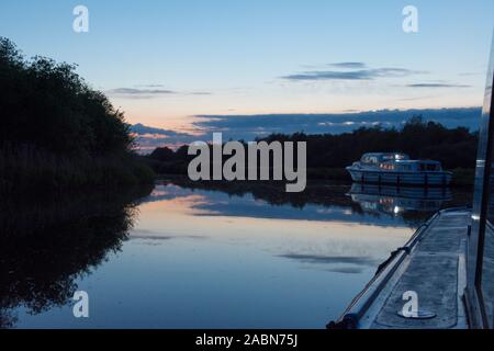 Vista serale di vacanza motor cruiser imbarcazioni ormeggiate fino per la notte sul telecomando in riva al fiume, tramonto, crepuscolo, Fiume Ant, Norfolk, maggio. Foto Stock