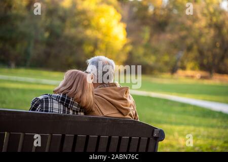 Romantico coppia senior è seduta sul banco in posizione di parcheggio e di godere di autunno. Foto Stock