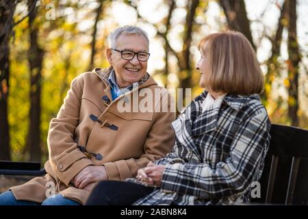 Coppia senior è seduta sul banco in posizione di parcheggio e di godere di autunno. Foto Stock