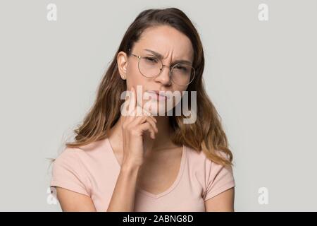 Malinconici dubbia donna che indossa gli occhiali di toccare il mento, pensando Foto Stock