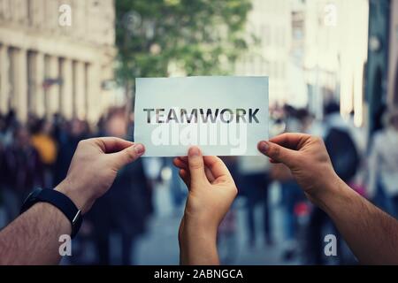 Diverse mani tenendo insieme una carta con il lavoro di squadra il testo. Un gruppo di tre persone unità e concetto di squadra come metafora di business per la giunzione di poteri. Partn Foto Stock