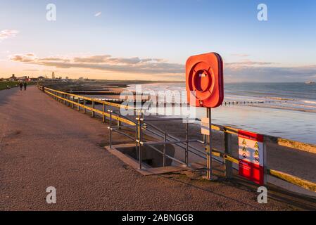 Salvagente su un sentiero recintato sul Seawall lungo una bellissima spiaggia al tramonto Foto Stock