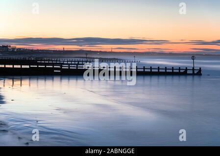 Vista di una spiaggia di sabbia con pennelli al crepuscolo Foto Stock