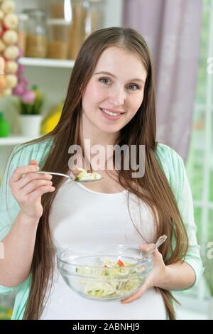 Sorridenti donna incinta mangiar sano insalata in cucina Foto Stock