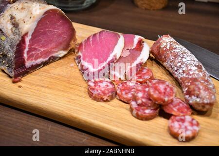 Fette di materie salati prosciutto casalingo o prosciutto e salsiccia su una tavola di legno con il coltello Foto Stock