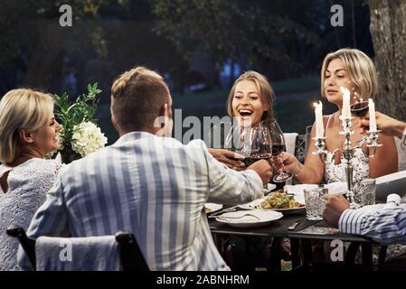 Ognuno è felice. Gruppo di amici adulti hanno un resto e la conversazione nel cortile del ristorante al tempo di sera Foto Stock