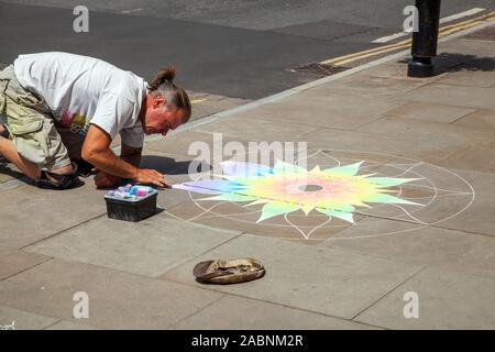 L'artista di strada raccogliendo denaro in un cappello facendo chalk artwork sul marciapiede in Somerset città di Glastonbury Inghilterra REGNO UNITO Foto Stock