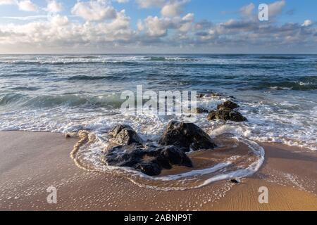 High surf e onde intorno le rocce vulcaniche su di una spiaggia di sabbia appena dopo il tramonto su una mattina nuvoloso con gara della luce del sole, Kapa'a Kauai, Hawaii Foto Stock