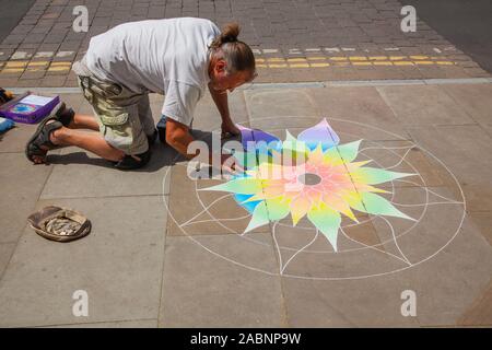 L'artista di strada raccogliendo denaro in un cappello facendo chalk artwork sul marciapiede in Somerset città di Glastonbury Inghilterra REGNO UNITO Foto Stock