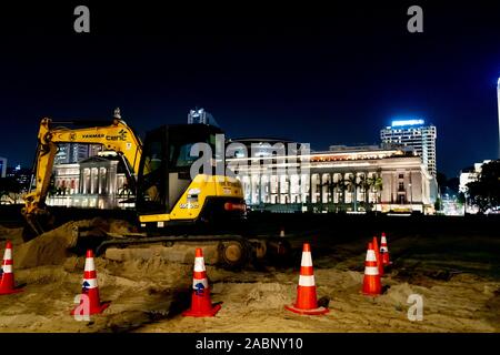 Giallo attrezzature da costruzione in piedi nella sabbia di fronte ad un edificio bellissimo di notte Foto Stock