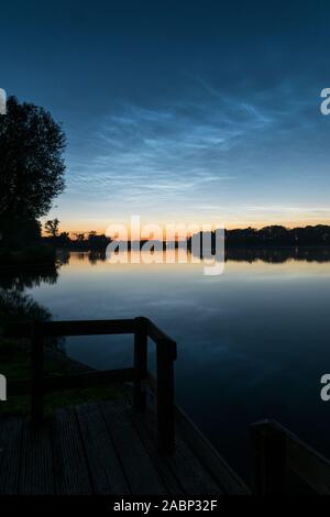 Scena tranquilla dopo il tramonto vicino alle calme acque di un lago con shining notte nuvole (NLC o noctilucent nuvole in cielo. Foto Stock