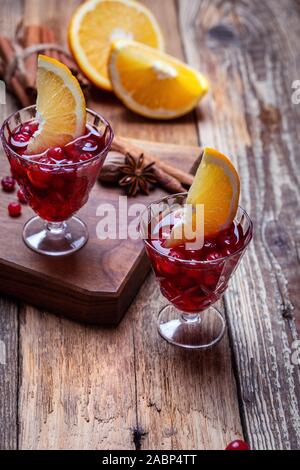 Vintage due bicchieri di vino brulé con mirtilli rossi, fettine di arancia e anice stellato su tavola in legno rustico, close up Foto Stock