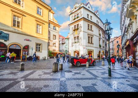 I turisti passeggiata, shop e gustare il caffè come essi passano da un rosso vintage automobile in una sezione di pittoresca della Città Vecchia di Praga, Repubblica Ceca. Foto Stock