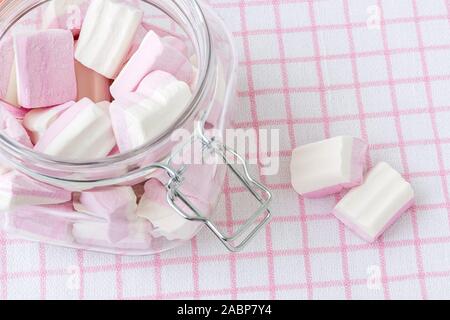 Bianco Rosa fluffy marshmallows in una clip top vasetto in vetro su una tovaglia a scacchi. Dolce e gustoso cibo d'inverno. Close-up deliziosi dolci morbidi. Foto Stock